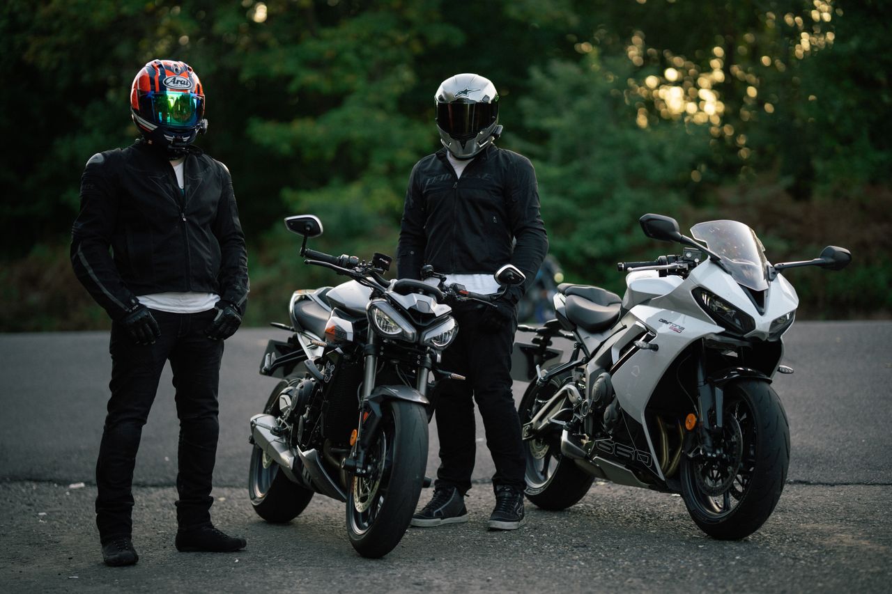 Two motorcyclists in gear, standing with their sport bikes on an open road